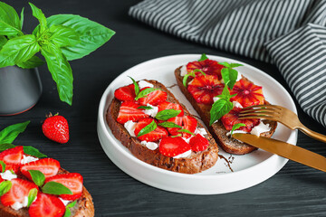 Tasty sandwiches with strawberry, blood orange, soft cheese and basil leaves on roasted wholegrain bread. Healthy delicious breakfast or lunch concept.