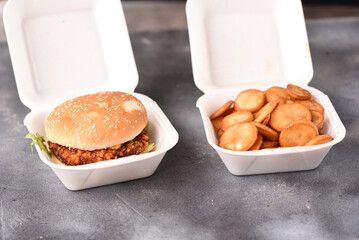 Crispy chicken burger in a plastic box
and golden fried potatoes. Delivered fast food.