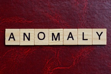 text the word anomaly from gray wooden small letters with black font on an red table