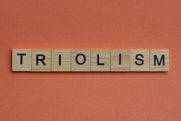 long word triolism from gray wooden small letters with black font on an orange background