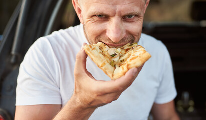 Close-up portrait of smilling man eating pizza. A guy dressed in a white T-shirt