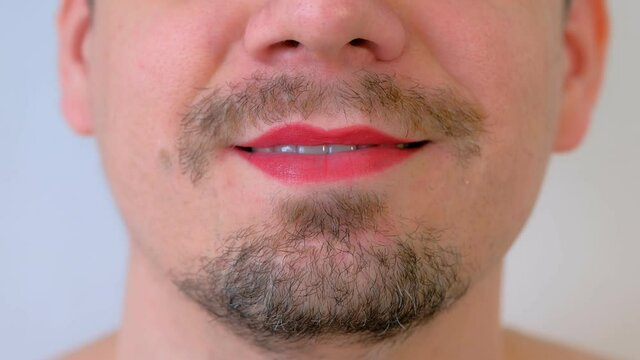 Man with red lipstick on lips giving a kiss on white background, mouth closeup. LGBT, gey, free love concept. Bearded unrecognizable young guy with moustache.