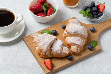 Croissants with fresh berries strawberries and blueberries, coffee cup. Traditional snack or breakfast. Delicious breakfast with fresh croissants and ripe berries, selective focus. 