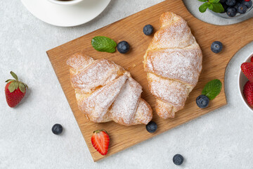Croissants with fresh berries strawberries and blueberries, coffee cup. Traditional snack or breakfast. Delicious breakfast with fresh croissants and ripe berries, selective focus. 