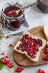 Top view of a sandwich with homemade jam or red currant jam on a wooden board and next to a jar of jam. Vertical orientation.