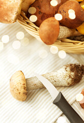 cooking and harvest concept - basket of different edible mushrooms, kitchen knife and towel on wooden table