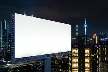 Obraz premium Blank white road billboard with KL cityscape background at night time. Street advertising poster, mock up, 3D rendering. Side view. The concept of marketing communication to promote or sell idea.