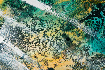 Colorful alcohol ink. Marble texture. Turquoise blue yellow stained surface with white paint strokes water drops streak grain black fleck effect. Mineral stone design art background.