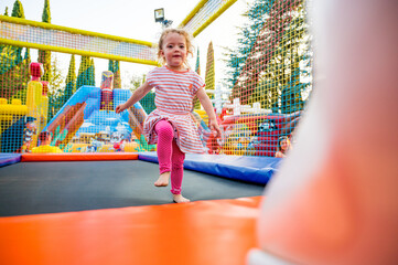 Fototapeta na wymiar Cute blonde girl jumping on big trampoline at outdoor playground.