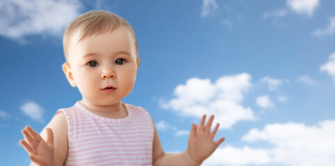 childhood and people concept - portrait of little baby girl over blue sky and clouds background