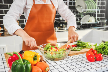 Vegetarian woman mixing vegetable salad in bowl while cooking in kitchen