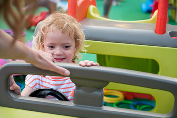 Fototapeta na wymiar Cute blonde girl riding a plastic car at outdoor playground.