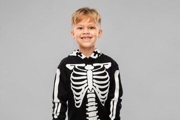 halloween, holiday and childhood concept - smiling boy in black costume with skeleton bones over grey background