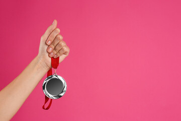 Woman holding silver medal on pink background, closeup. Space for design