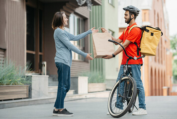 Courier with bicycle delivered shopping bag to client. Smiling girl takes bag from man in helmet...
