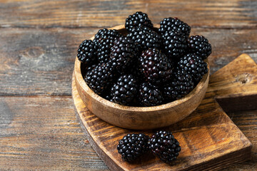 Blackberries in a wooden bowl on a brown wooden table. Fresh blackberries in a bowl close-up. Space for text