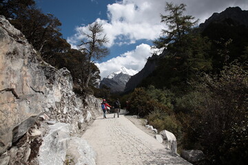 Fototapeta na wymiar Tourists walking to Yading Nature Reserve with the sacred Mount Chanadorje (Chinese: Xianuoduoji) during Autumn at Shangri-La region in Daocheng county, southwest of Sichuan Province, China.