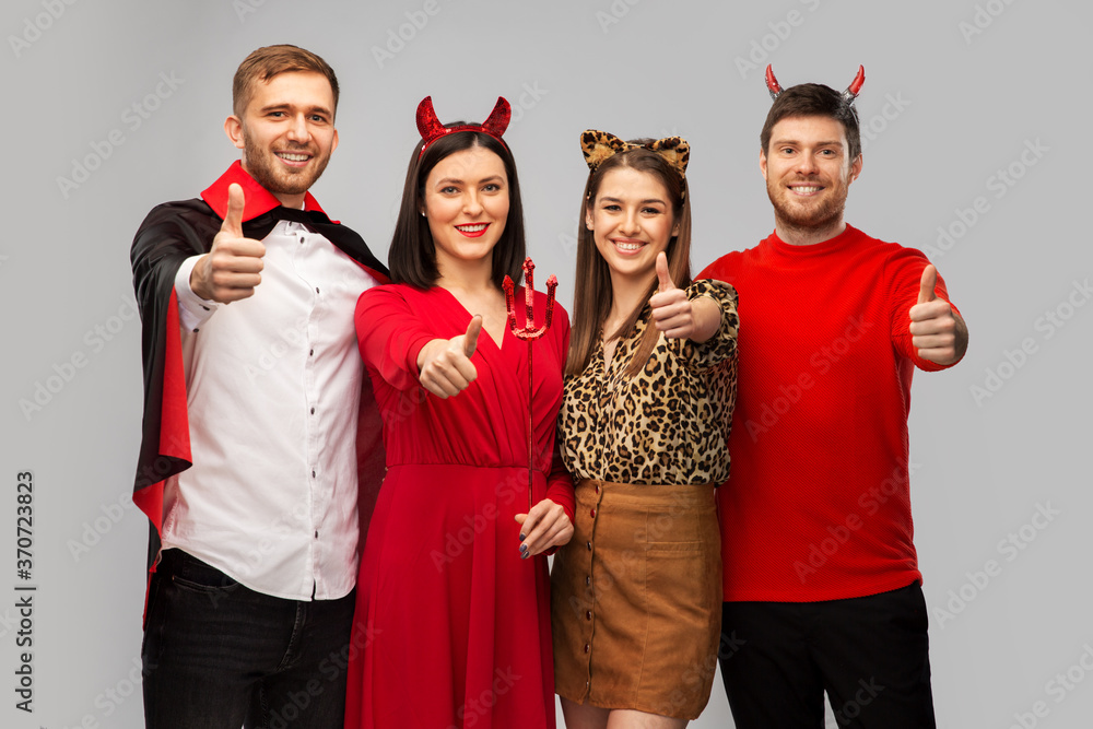 Sticker friendship, holiday and people concept - group of happy smiling friends in halloween costumes of vampire, devil and cheetah showing thumbs up over grey background