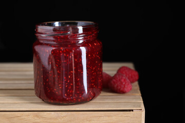 Delicious jam and fresh raspberries on wooden crate, closeup. Space for text