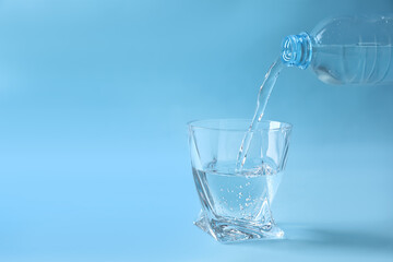 Pouring water from bottle into glass on light blue background. Space for text