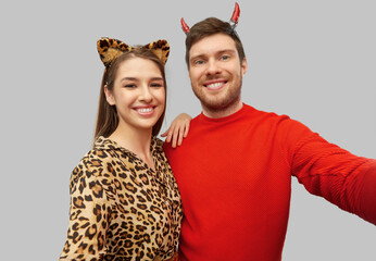 holiday and people concept - happy smiling couple in halloween costumes of devil and leopard taking...