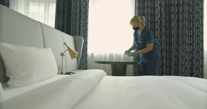 The Maid In A Mask And Gloves Disinfects The Hotel Room. Cleaning And Disinfection Of Furniture. Cleaning In A Hotel Room Or At Home.