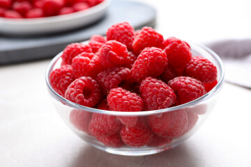 Delicious fresh ripe raspberries in glass bowl on white table, closeup