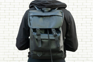 Close up of eco leather black backpack on mans back with white brick wall background