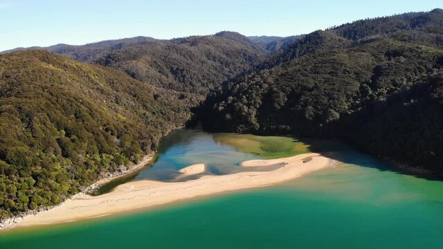Sandy beach across Sandfly Bay aerial fly backward shot reveal of beautiful landscape of Abel Tasman. Coast shaped by mountains covered in jungle forrest.