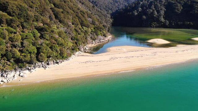 Remote beach across a bay in the jungle paradise aerial fly sideway shot. Beautiful coastline of New Zealand.