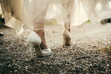 Closeup bride shoes walking on a gravel path at sunset light.