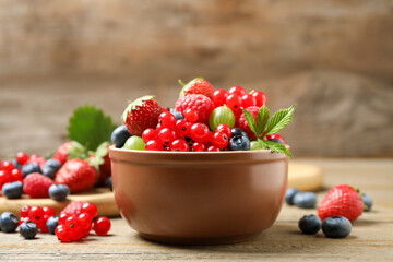 Mix of different fresh berries in bowl on wooden table