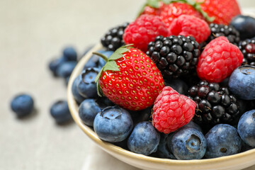 Mix of different fresh berries in bowl on light grey table, closeup