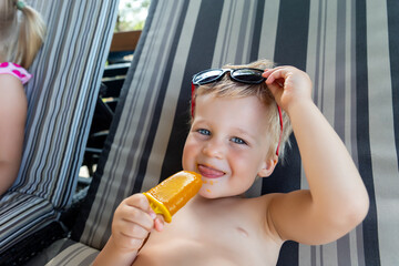 Two cute adorable caucasian blond little siblings enjoy having fun relaxing and eat fruit popsicle...
