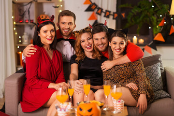 friendship, holiday and people concept - group of happy smiling friends in halloween costumes of vampire, devil, witch and cheetah at home party at night