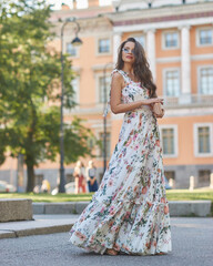 Young beautiful woman wearing white dress with floral prink and walking at city street between...