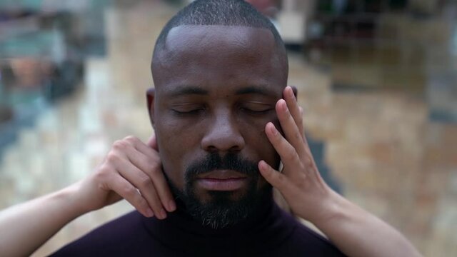hands of white woman are stroking head of black man, closeup male portrait