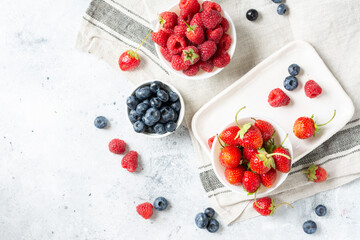 Ripe berries. Different berries in white ceramic bowls on a light table. Strawberries, raspberries and blueberries in plates against a white brick wall. Top view with space for text