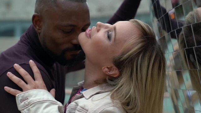 black man is kissing in neck his beloved girlfriend on street in downtown, white woman is enjoying