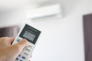 Hand with remote control directed on air conditioner inside the room