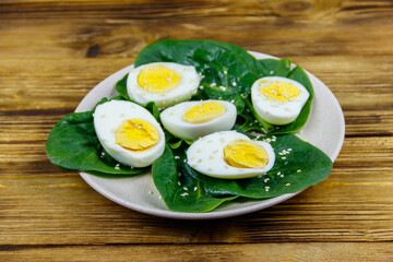 Boiled eggs with fresh spinach leaves and sesame seeds on wooden table