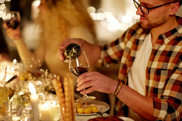 holidays and celebration concept - man pouring red wine into glass at christmas party