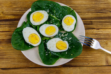 Boiled eggs with fresh spinach leaves and sesame seeds on wooden table. Top view