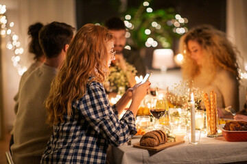 holidays and people concept - woman with smartphone at dinner party with friends at home