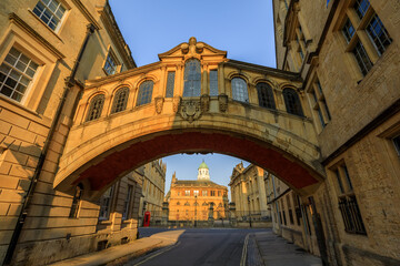 Hertford Bridge, Bridge of Sighs, in Oxford at sunrise with Sheldonian Theatre behind it and no people around, early in the morning on a clear day with blue sky. Oxford, England, UK.