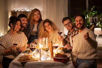 holidays, celebration and people concept - happy friends taking with smartphone on selfie stick at home christmas dinner party