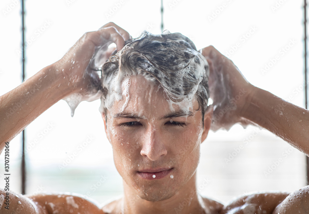 Wall mural handsome young man washing hair with shampoo