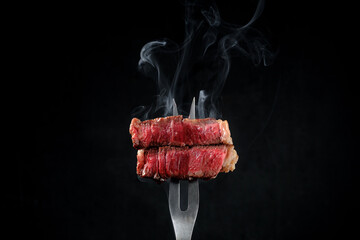 Sliced and steaming rare rib eye steak on a fork on a dark background