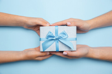 Human's hand holding a present, gift, surprise box isolated on blue background. Concept of celebration, holidays, family, home comfort, winter's holidays, New Year eve, birthday, anniversary