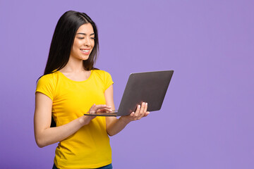 Naklejka premium Online Education. Smiling Asian Girl Using Laptop Computer Over Purple Background